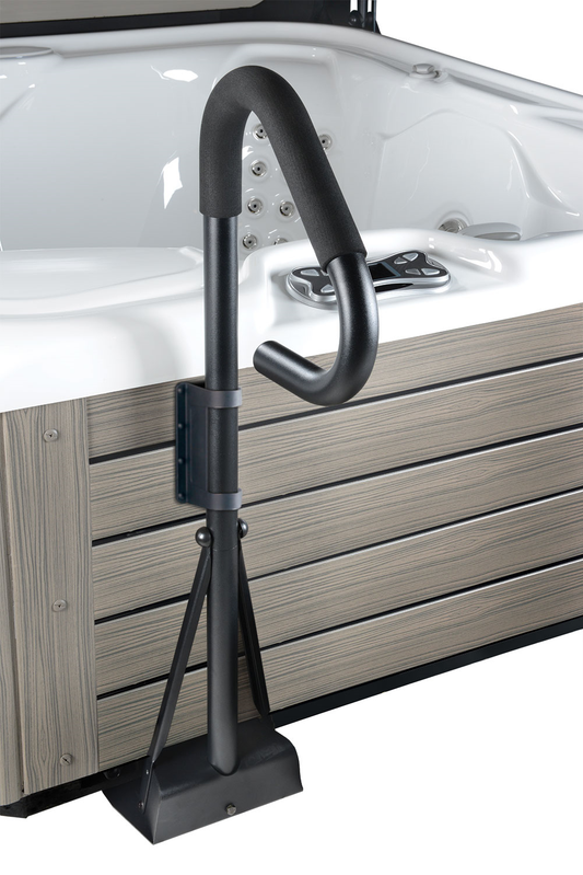 A black, metal railing with a foam grip, mounted on a wooden spa surround with a pool and spa in the background.
